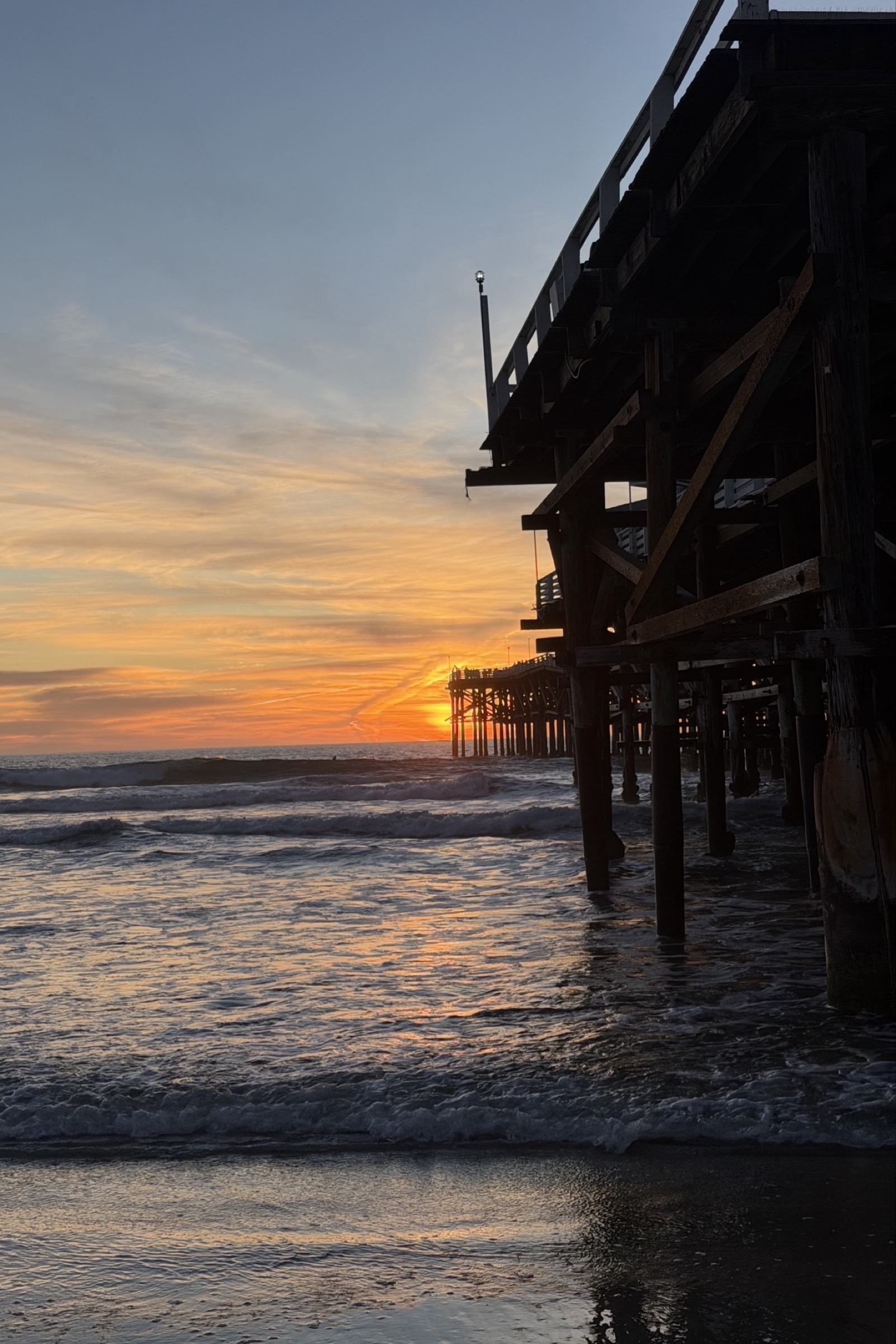 The underside of Crystal Pier from the sand, pilings receding toward the setting sun.