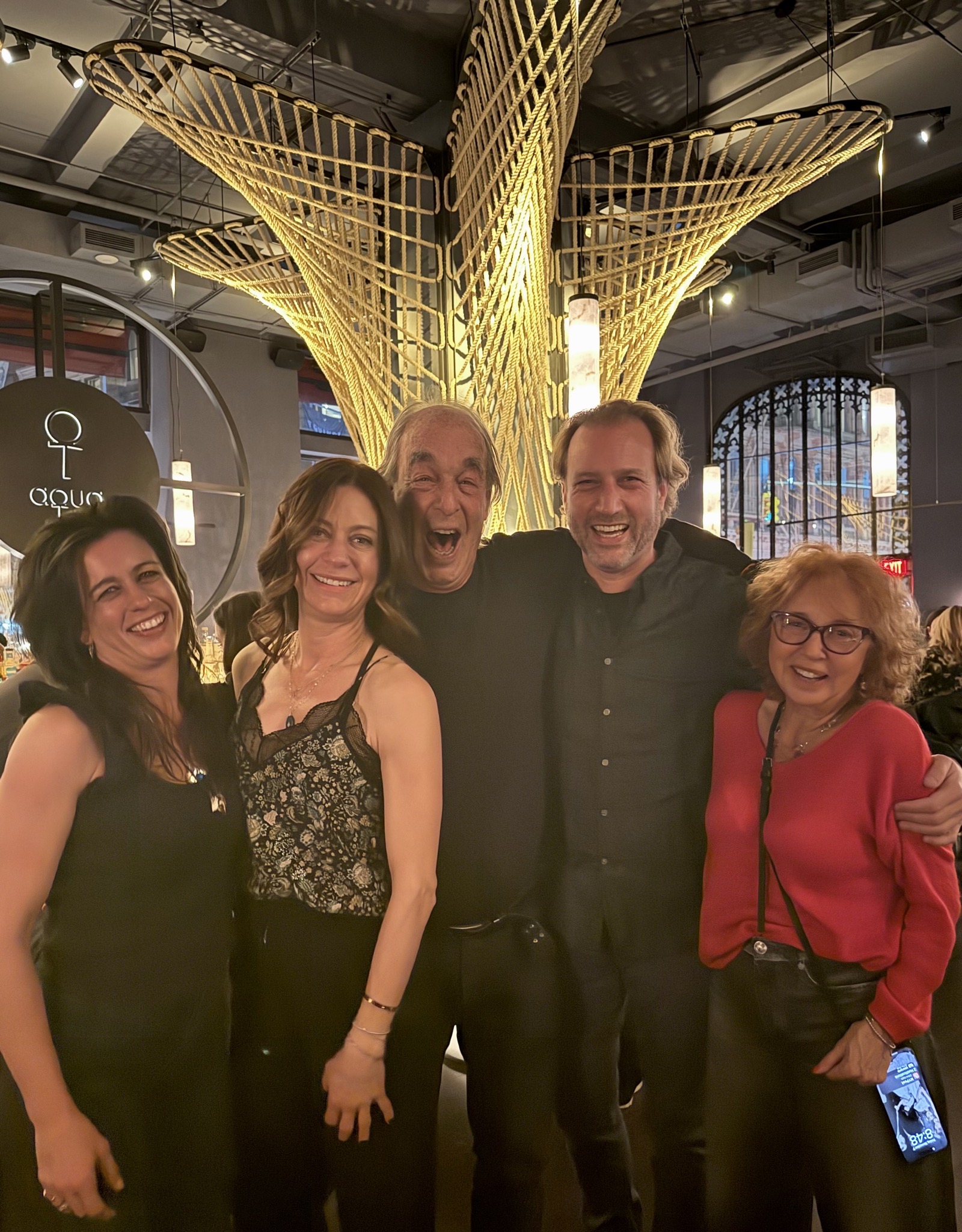 Five family members standing together and laughing under a lit rope sculpture in a restaurant.